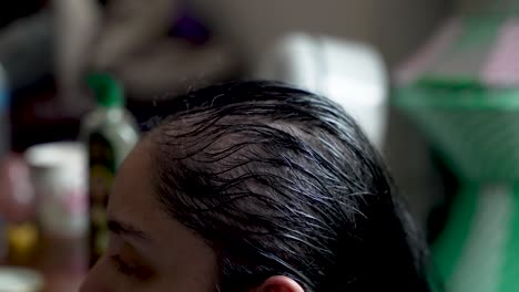 close-up of hands applying oil to a person's hair, emphasizing the texture and shine