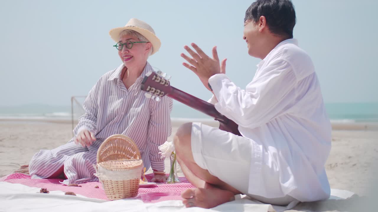 여름에 바가에서 휴식을 취하는 아시아의 은퇴 한 부부는 해변에서 파트너와 함께 피크닉을 할 때 기타를 연주하는 고령자입니다.