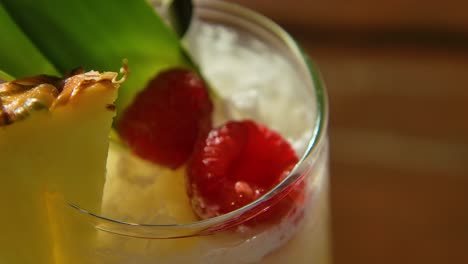 Primer-Plano-De-Foco-De-Cóctel-De-Piña-Colada-En-La-Mesa,-Con-Frambuesas-Y-Piña