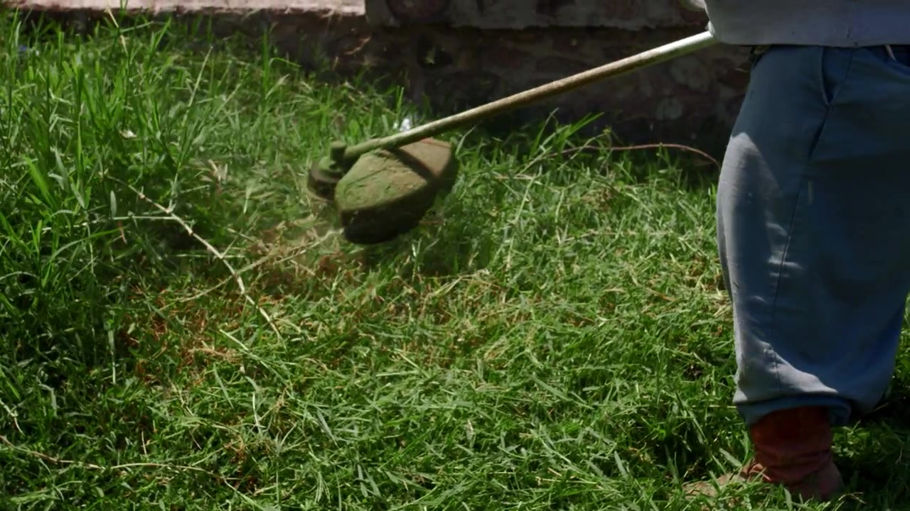 Close-up de jardineiro aparando grama crescida com roçadeira a gasolina