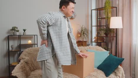 man carrying heavy box and experiences severe back pain sitting on sofa in living room at home