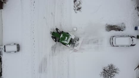 green snow plow tractor cleaning suburb streets of canada, aerial top down view