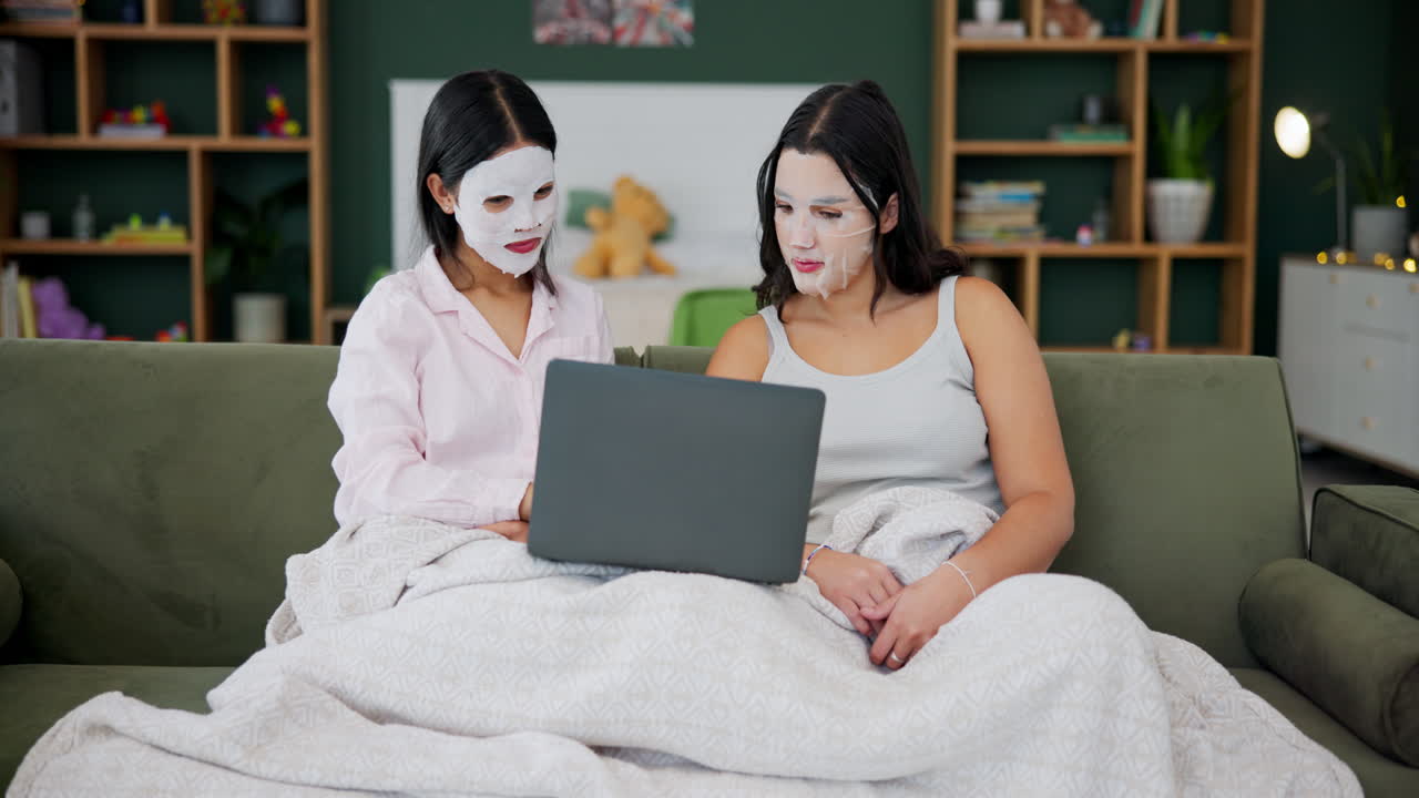 Two women with face masks using a laptop on the couch