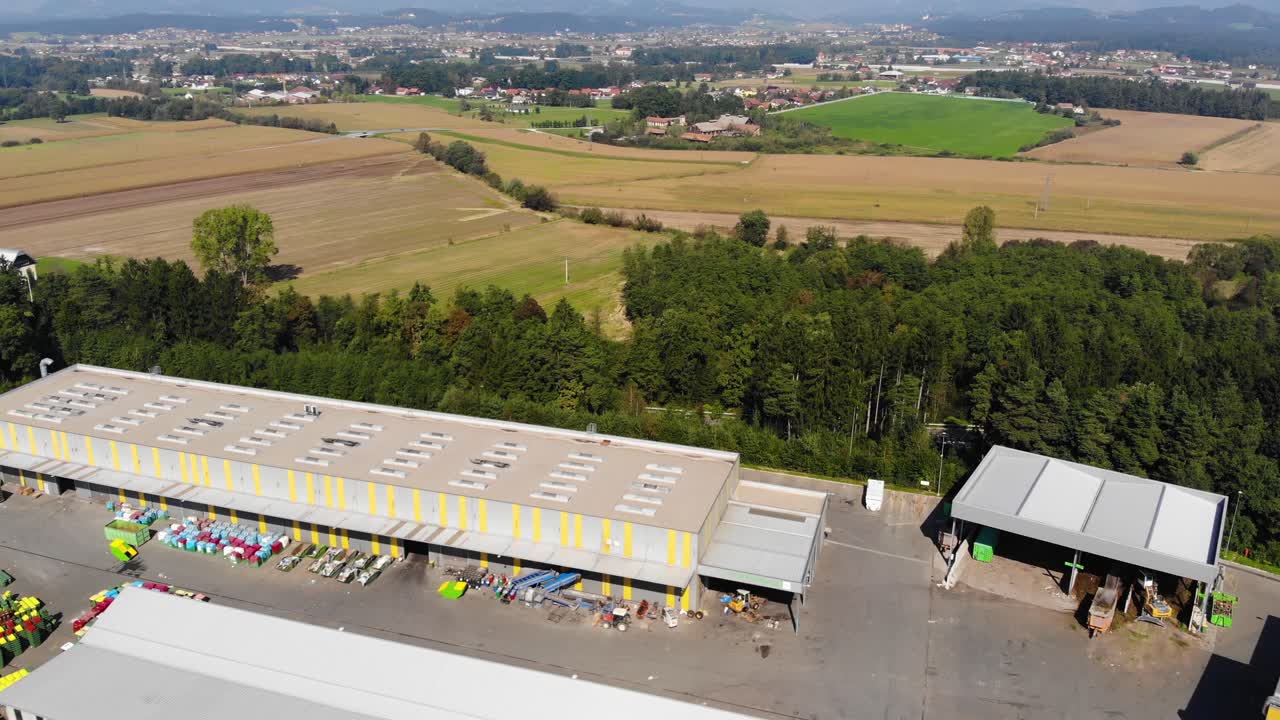 Industrial recycling plant for plastic materials near farm fields in easter Europe, Aerial pan left reveal shot