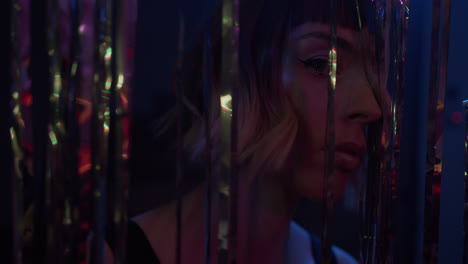 a young woman stares int the camera through glittering curtain