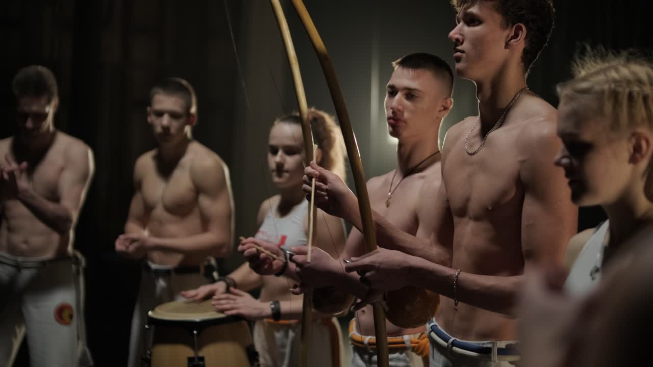 группа профессиональных танцоров практикует капоэйру в темноте под прожектором на черном фоне студии. афро-бразильское боевое искусство, которое сочетает в себе элементы танца.