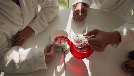 man pours tea into woman cup at table closeup. loving boyfriend takes care of girlfriend sharing delicious drink in morning. romantic relationship joy