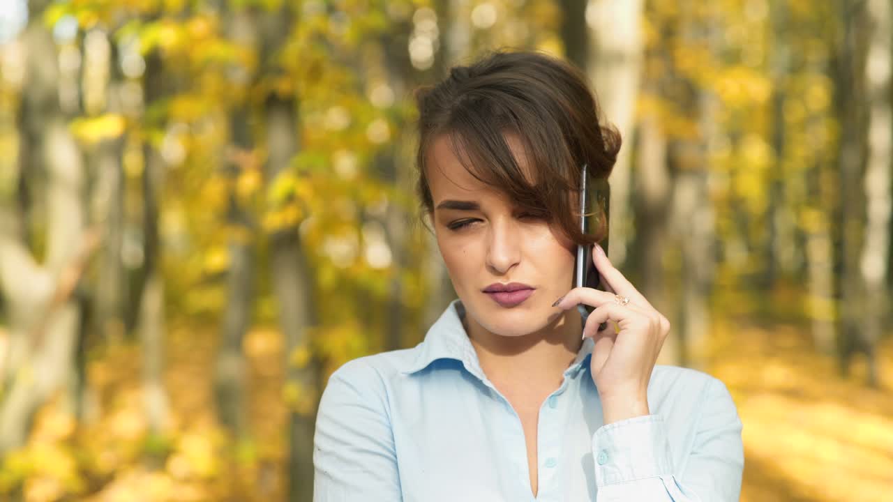 Woman with cellphone in park. Girl speaking on mobile phone in the autumn forest