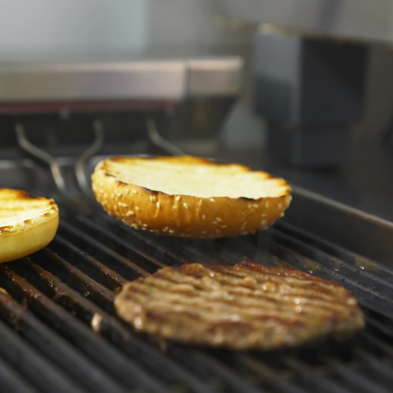 Side view of the delicious burger cutlet and two buns flipped on the grill with hand in latex gloves. Selective focus
