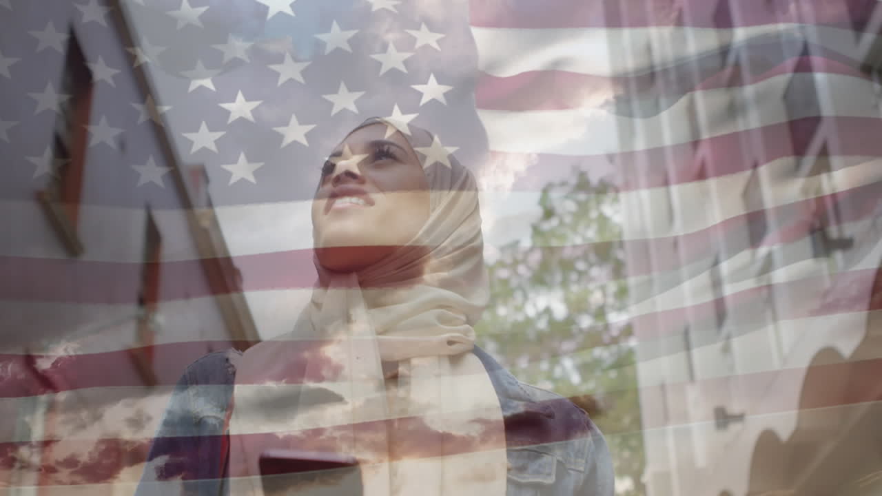 Animation of American flag waving over woman in hijab walking holding smartphone