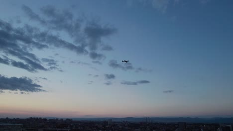 aerial-drone-showing-Commercial-airplane-flying-over-Sofia-city-skyline,-Bulgaria,-dusk,-tilt-down-reveal-from-the-air
