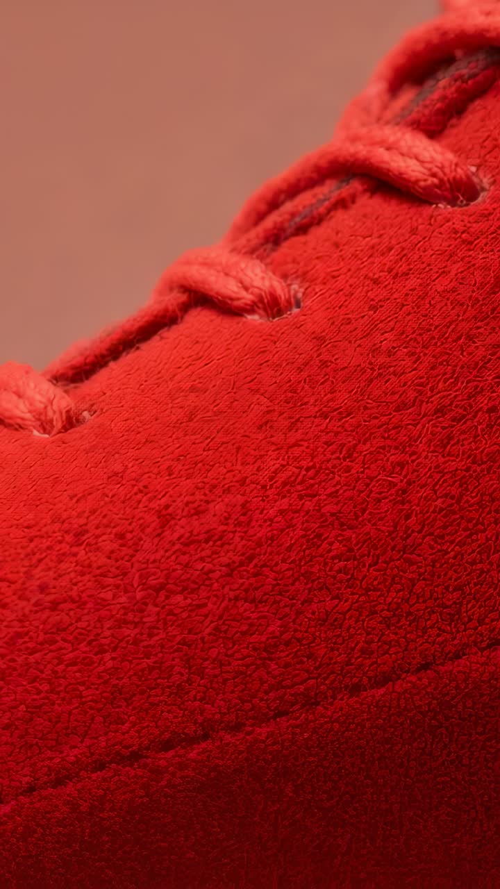 Vertical video: Pushing camera over red suede upper in studio, revealing braided laces, showing nap