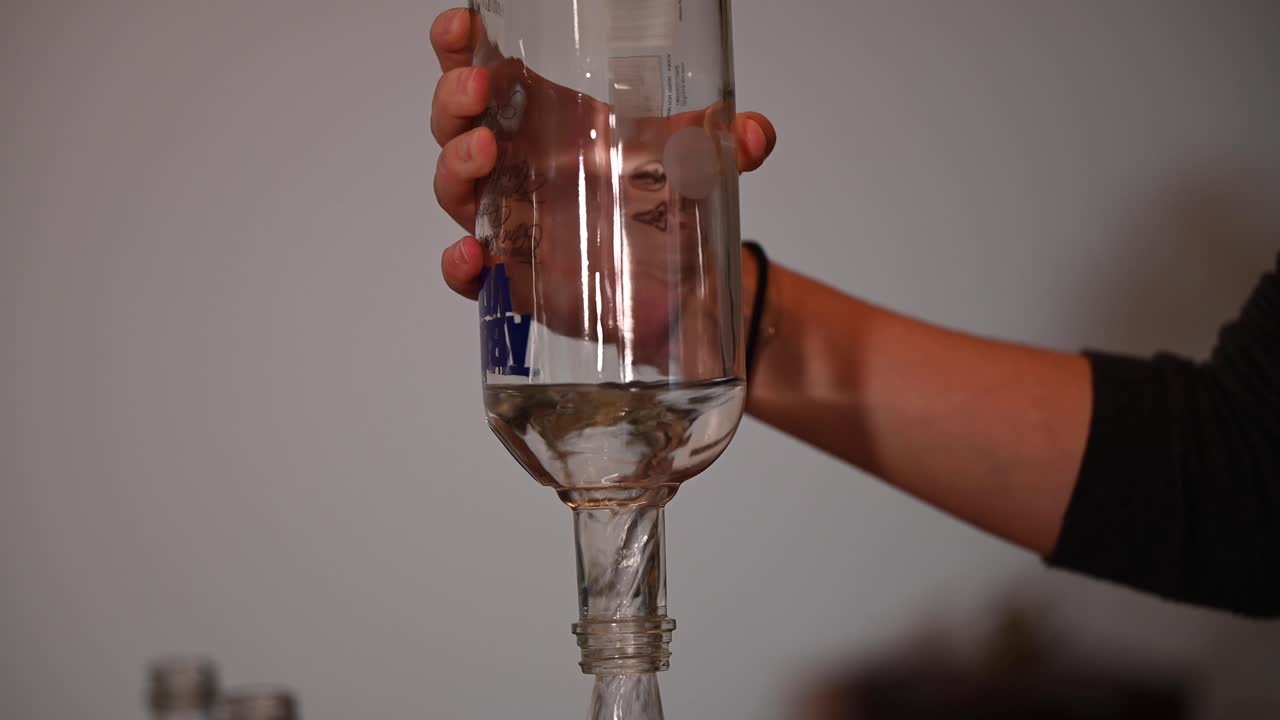 una toma estacionaria de la mano de una mujer mientras vierte vodka hasta la última gota