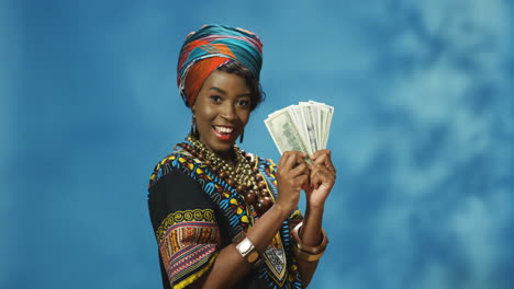 african american young woman in turban and traditional clothes holding money and looking at camera