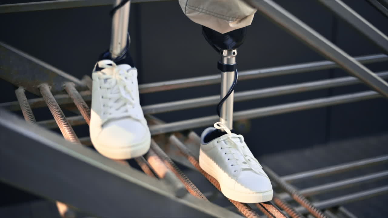 Slow motion view of a man with prosthetic legs and white sneakers staying on a metal staircase