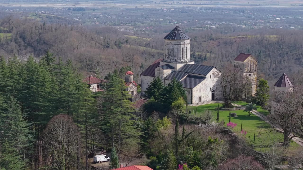 Aerial view of Martvili Monastery perched on a hill, surrounded by a striking mix of evergreen and leafless deciduous trees during the early spring season.