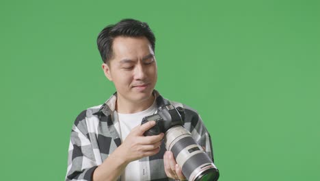 close up of asian photographer taking pictures then looking at them in the camera while standing on green screen background in the studio