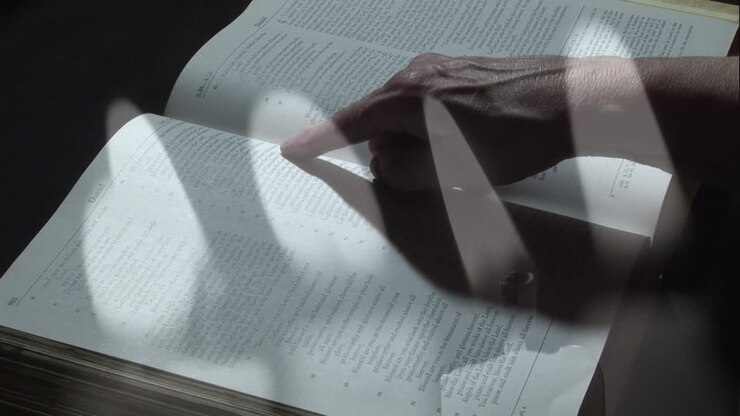 Burning candles against hands reading bible