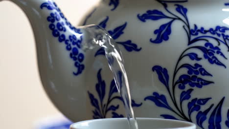 pouring water into a tea cup from a decorated teapot