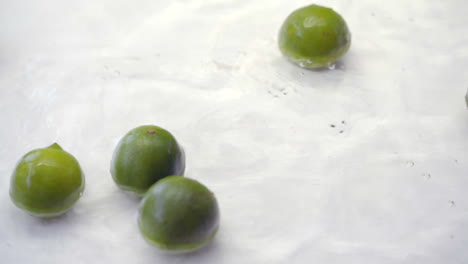 slomo de limas cayendo al agua sobre fondo blanco