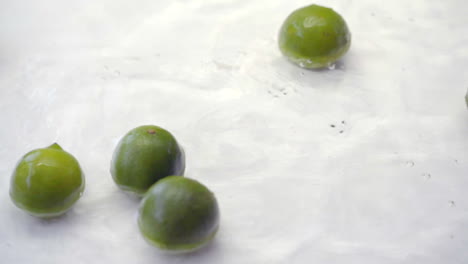 slomo of limes falling into water on white backdrop