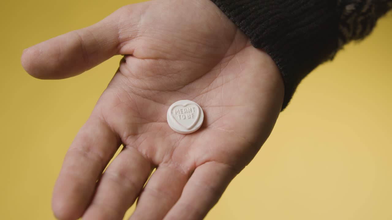 primer plano de la mano que sostiene el caramelo del corazón con el mensaje destinado a ser sobre fondo amarillo