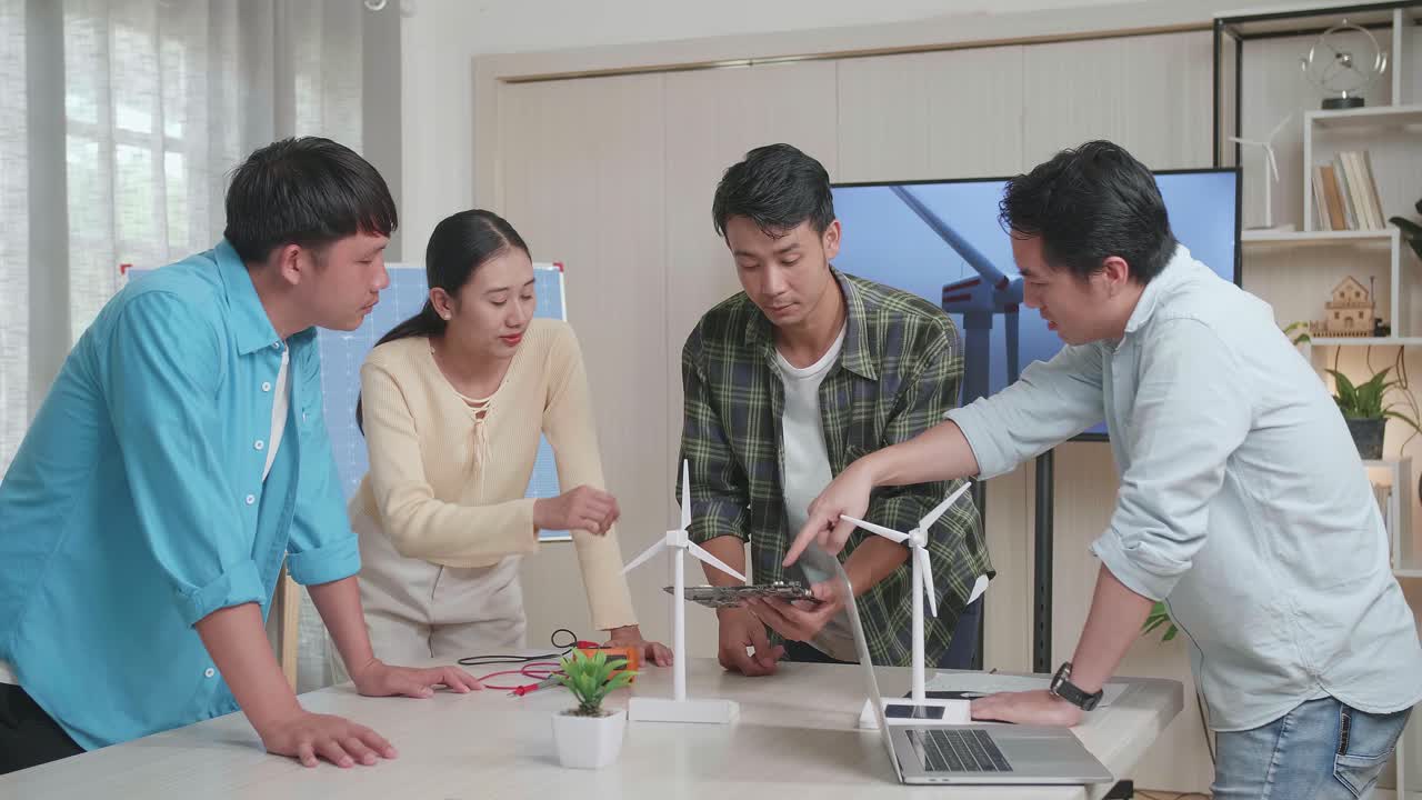 풍력 터빈과 태양전지를 가진 아시아 엔지니어 그룹이 사무실에서 녹색 회로 보드에 대한 회의를 하고 있습니다.