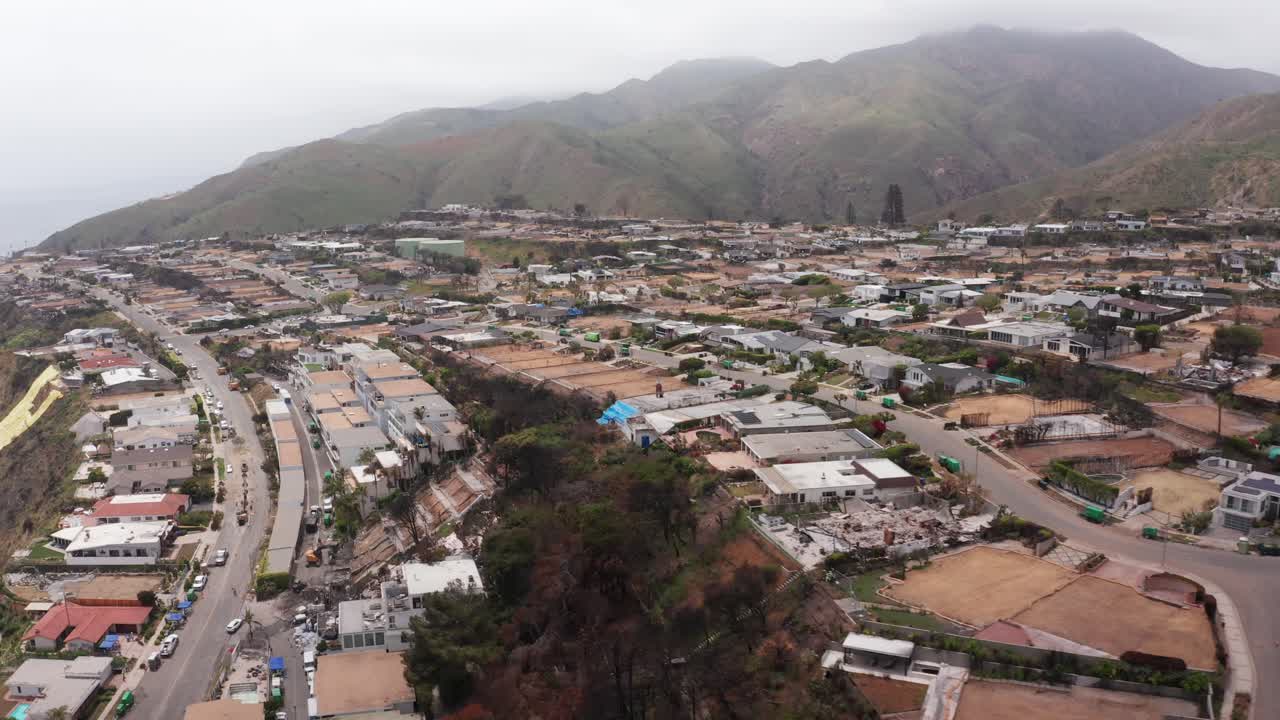 Aerial rising dolly shot of burned residential lots in the oceanfront Sunset Mesa neighborhood after the Palisades wildfire in Malibu, California. 4K