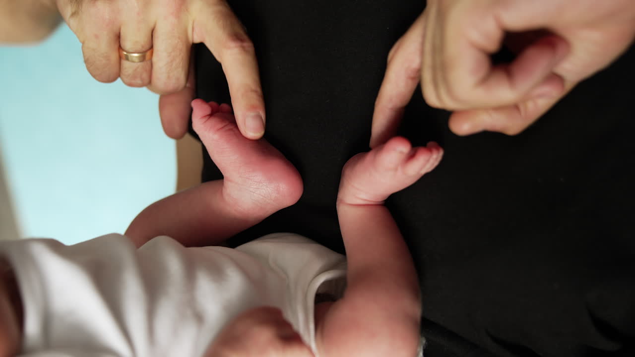 Male hands tickling tiny newborn's feet. Father is playing with his baby. Close up.