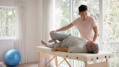 diverse male physiotherapist advising and senior male patient stretching, in slow motion