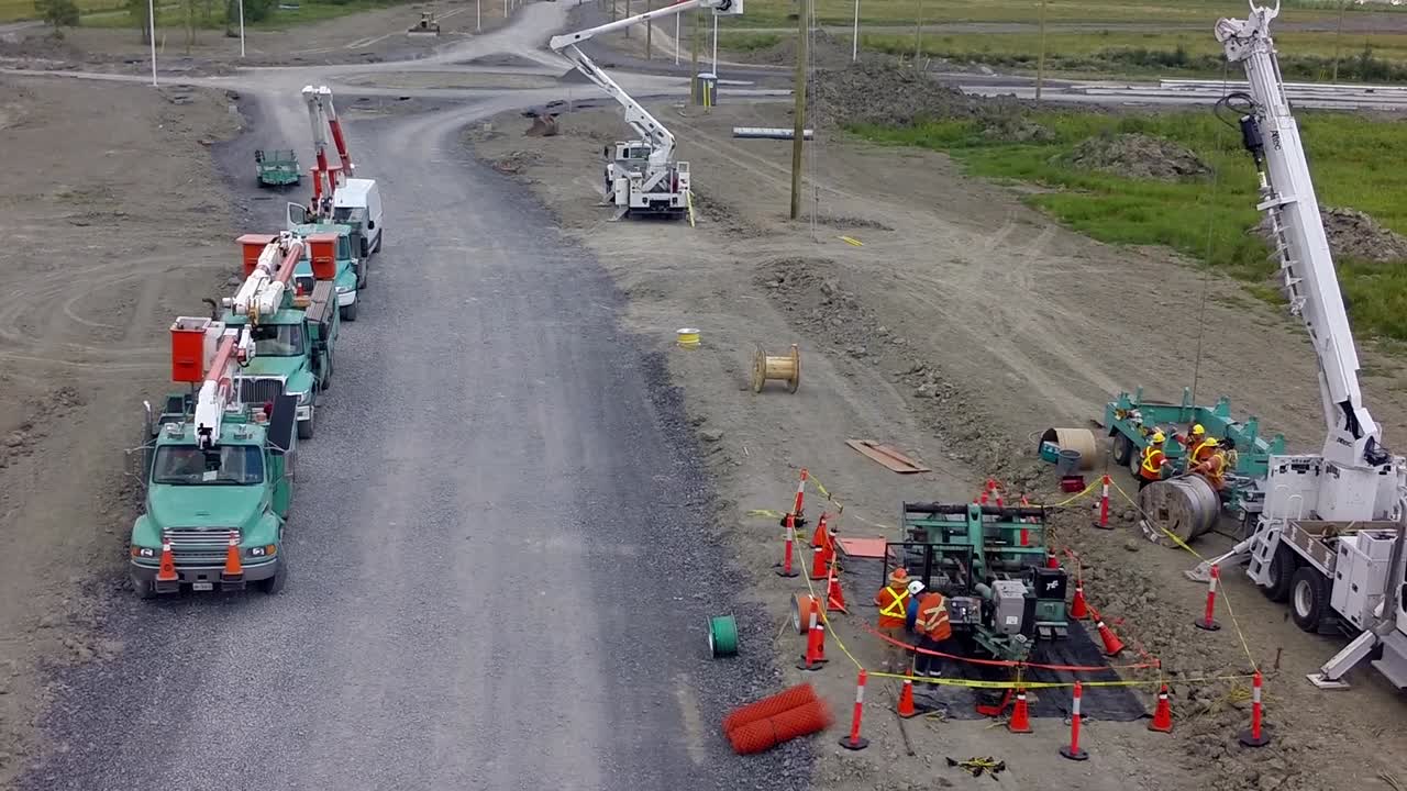 Electrical wires and poles being installed by many trucks along a new built road