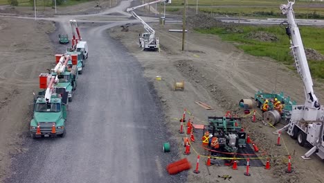 electrical wires and poles being installed by many trucks along a new built road