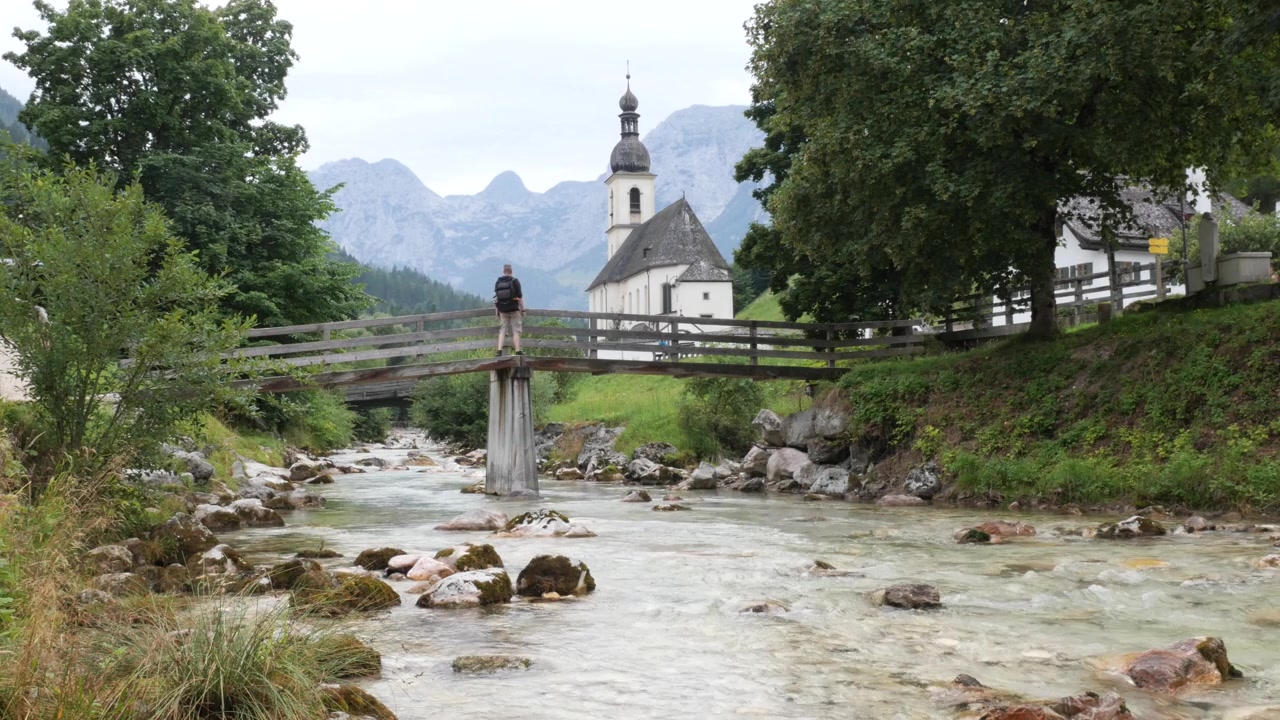 Homme traversant un pont en bois en direction de l'église Saint-Sébastien à Ramsau, Bavière, Allemagne.