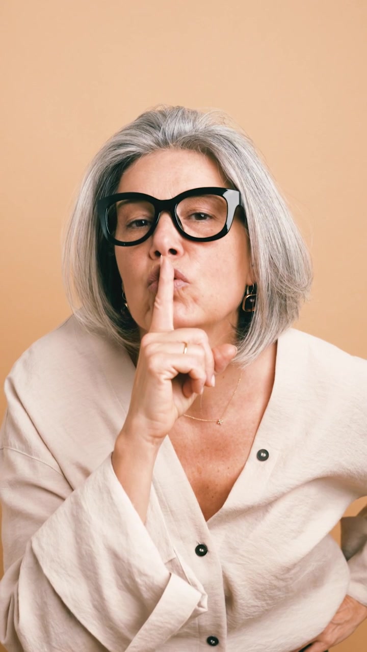 Donna matura che fa un gesto discreto su uno sfondo neutro