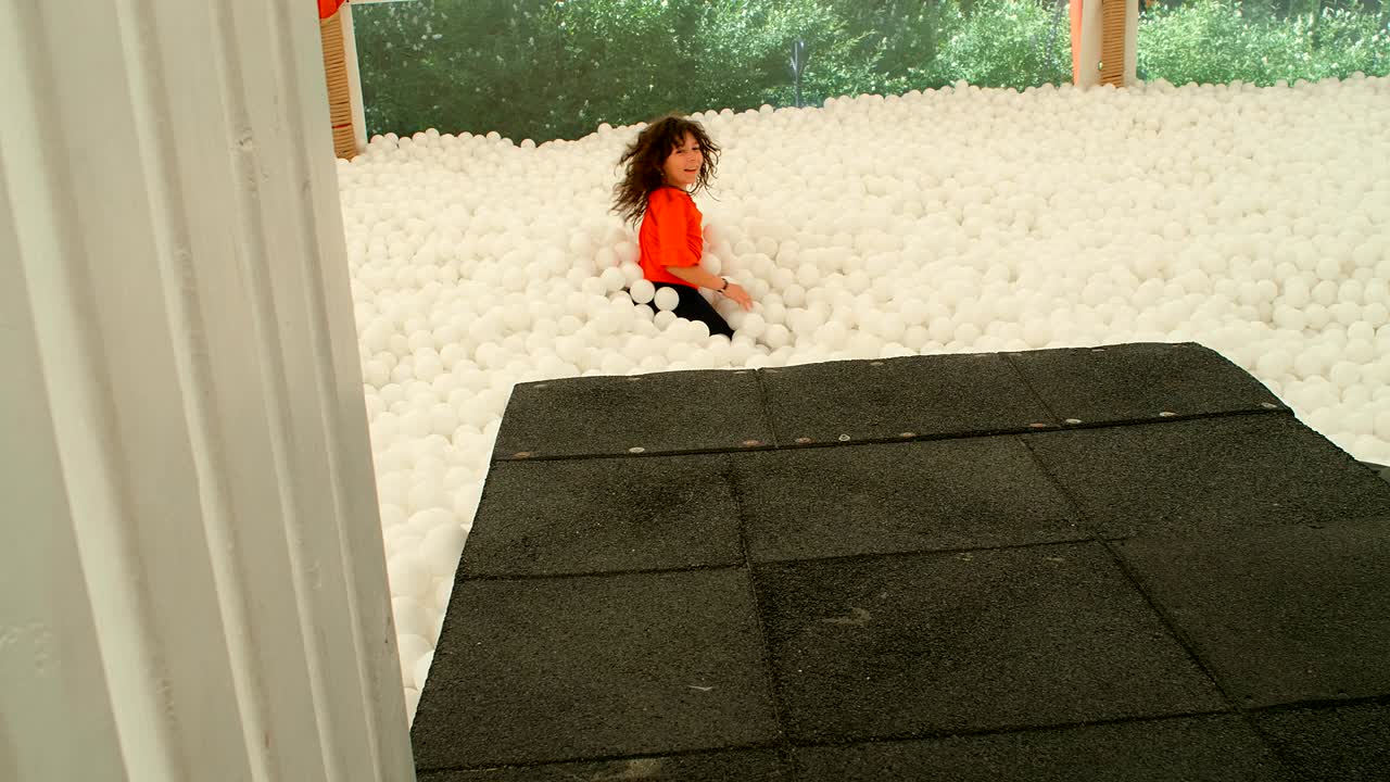 9~10살의 귀여운 소녀가 공 구이에 있는 많은  공들 사이에서 즐거움을 즐기고 있다.