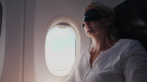 a young woman with a dark bandage in her eyes sleeps in the cabin of a passenger aircraft traveling