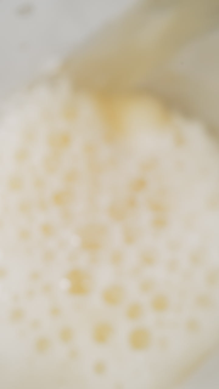 Pouring fresh beer with fluffy froth into glass macro upper view. Swirling flow of organic alcohol drink with bubbling foam slow motion