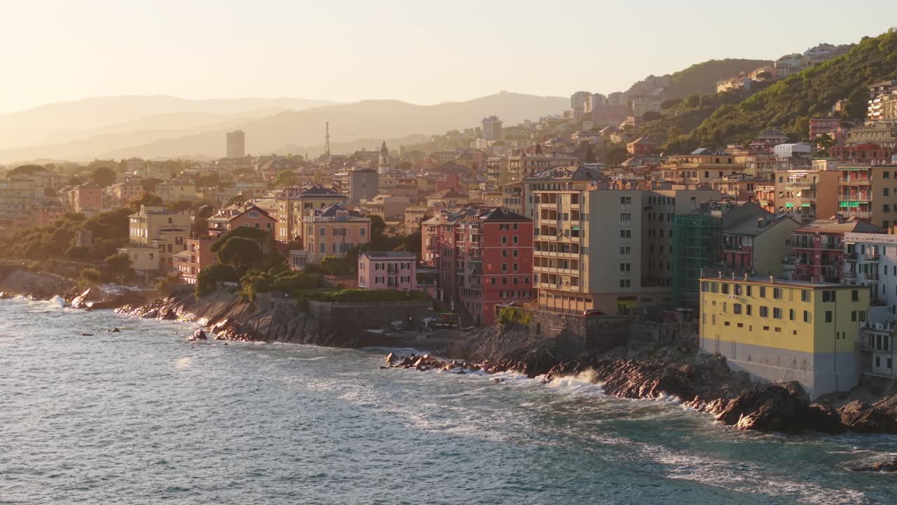 Golden hour sunset over coastal city with buildings and rocky shoreline, aerial view