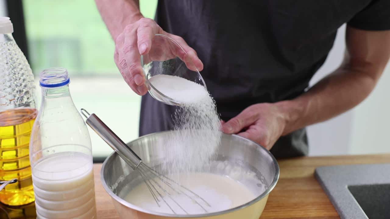 Person pouring sugar into a mixing bowl during food preparation
