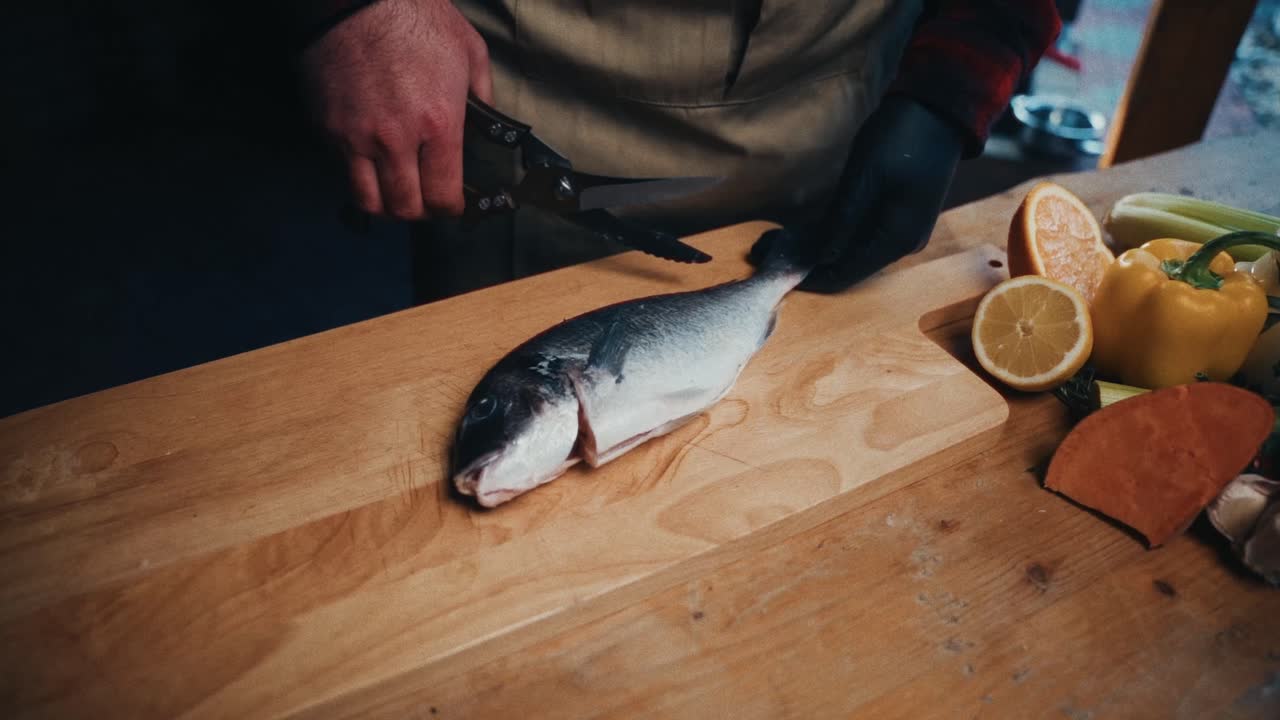 una persona limpia un pez en una tabla de madera con verduras frescas cerca
