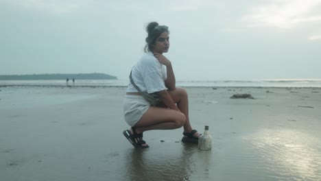 a young girl, crouched on the beach, looks directly at the camera