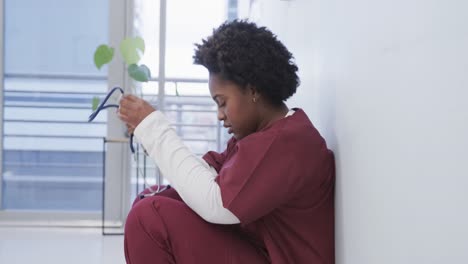 Tired-african-american-female-doctor-squatting-in-hospital-corridor,-slow-motion