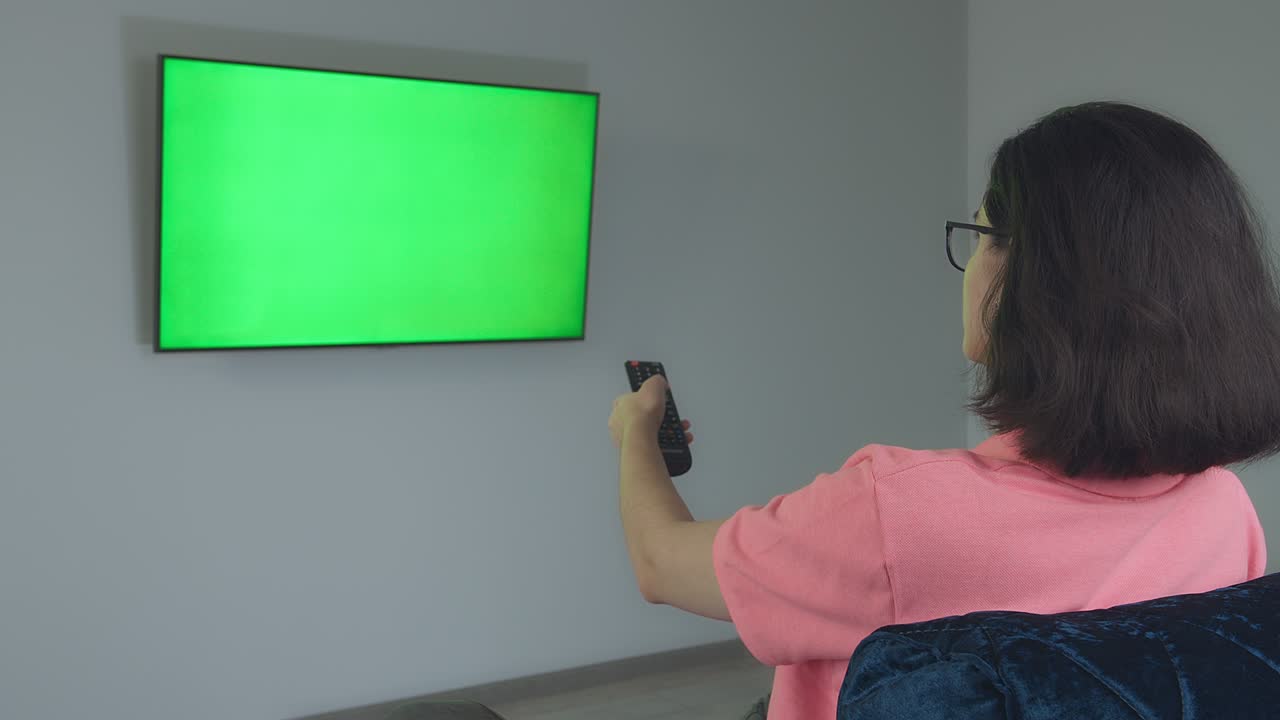 tv colgada en la pared, una chica sentada en el sofá y cambiando canales con el control remoto, chromakey
