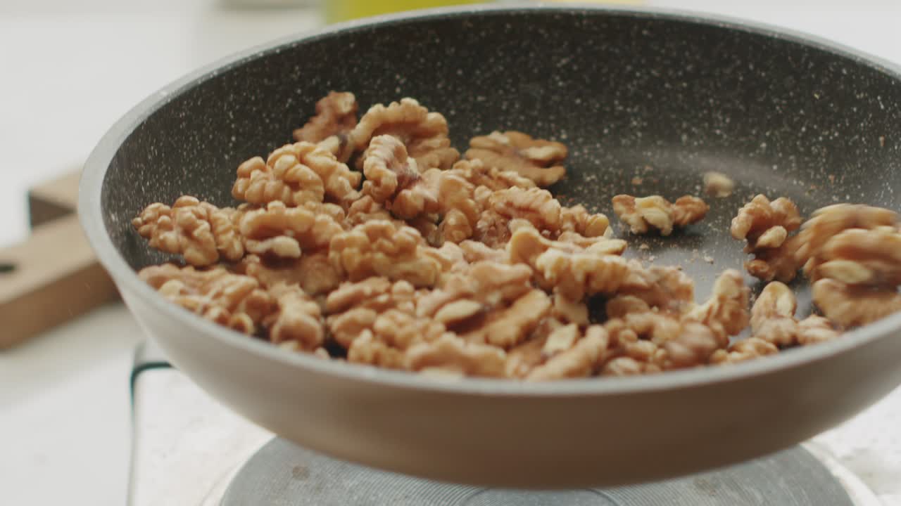 Anonymous person frying walnuts in pan in kitchen
