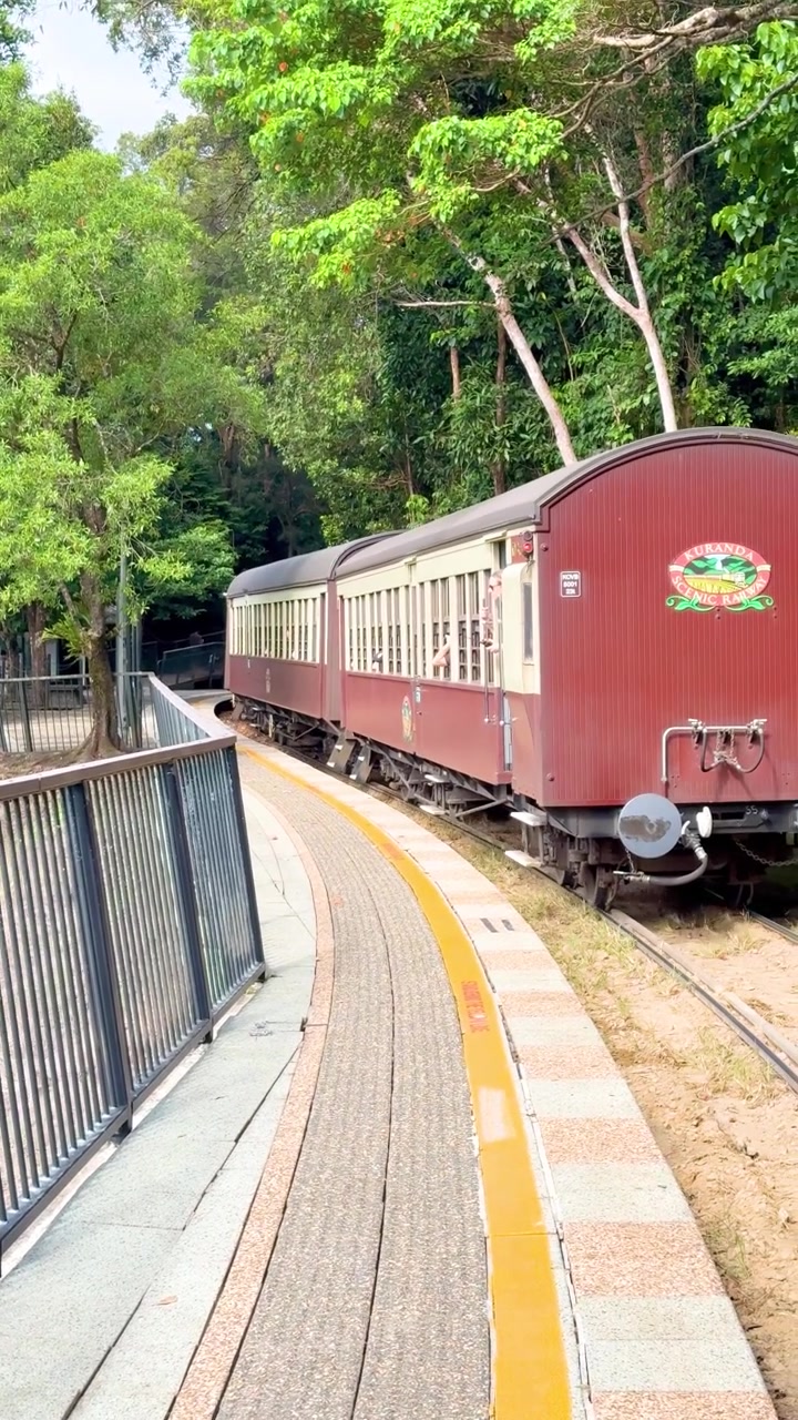 Treno classico bordeaux lascia lentamente la stazione forestale, luce diurna intensa, vegetazione lussureggiante, panoramica fluida della telecamera.