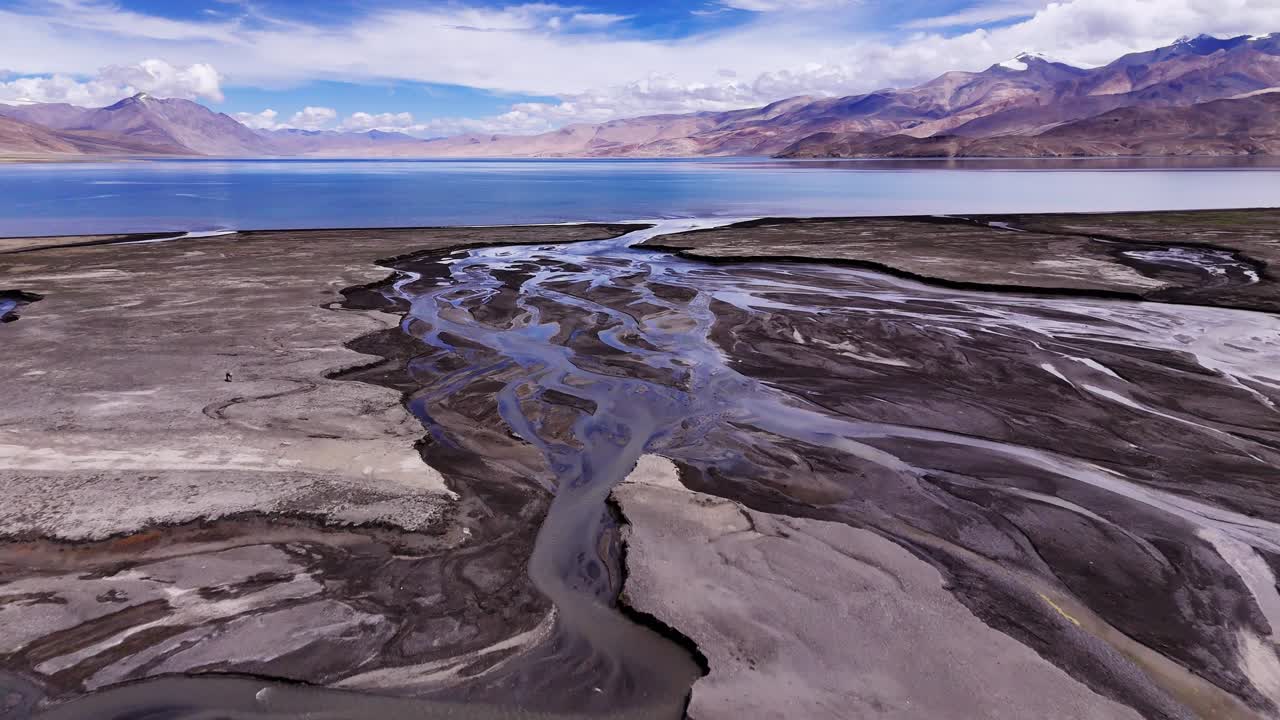 Melting icy water creating abstract curvy stream as it meanders over glacial flat stony lands to mountain lake. Drone reveal surreal patterns in river bed