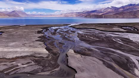 melting icy water creating abstract curvy stream as it meanders over glacial flat stony lands to mountain lake. drone reveal surreal patterns in river bed