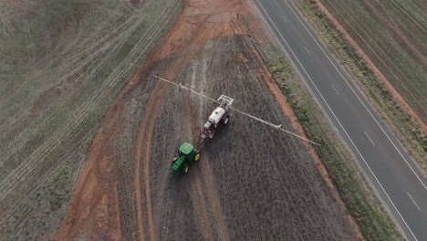 Drone-birds-eye-view-of-farming-tractor-driving-across-empty-field-about-to-start-work