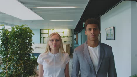 multiethnic coworking man and woman in office. young blond woman and african-american man in suit standing together in office looking at camera