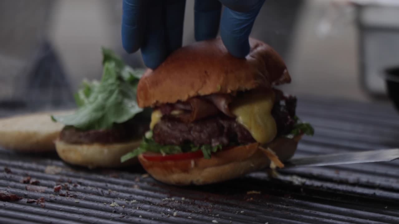 Uno chef finisce di cucinare un hamburger di carne con lattuga, pomodoro e formaggio fuso sulla griglia.